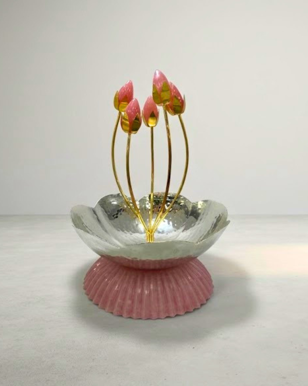 A decorative lotus-shaped dish with a pink ribbed base, a silver metallic inner bowl, and five gold stems holding pink and green lotus bud ornaments, set against a plain light gray background.