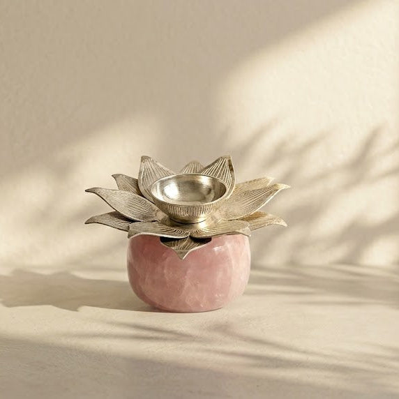 A small decorative lotus-shaped candle holder with a metallic silver top and a pink marble base, styled on a light beige surface with soft window shadows.