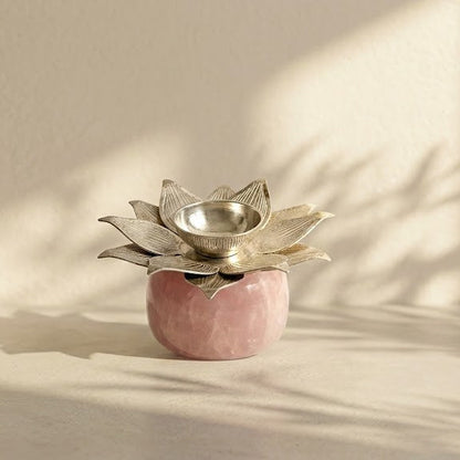 A small decorative lotus-shaped candle holder with a metallic silver top and a pink marble base, styled on a light beige surface with soft window shadows.