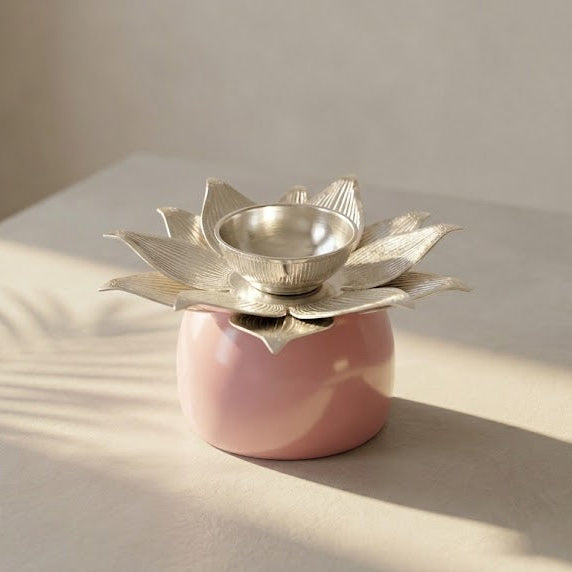 A pink ceramic candle holder with a metallic silver lotus flower top holding a small silver bowl, set on a light beige surface with soft shadows.