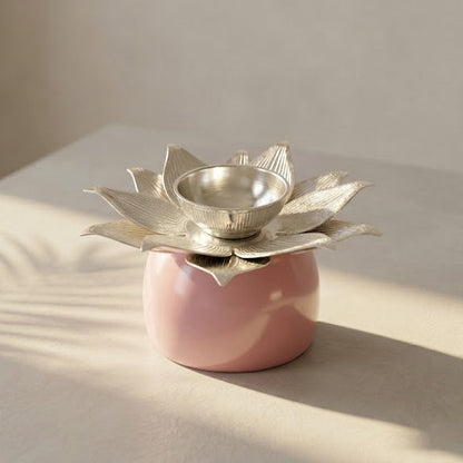 A pink ceramic candle holder with a metallic silver lotus flower top holding a small silver bowl, set on a light beige surface with soft shadows.