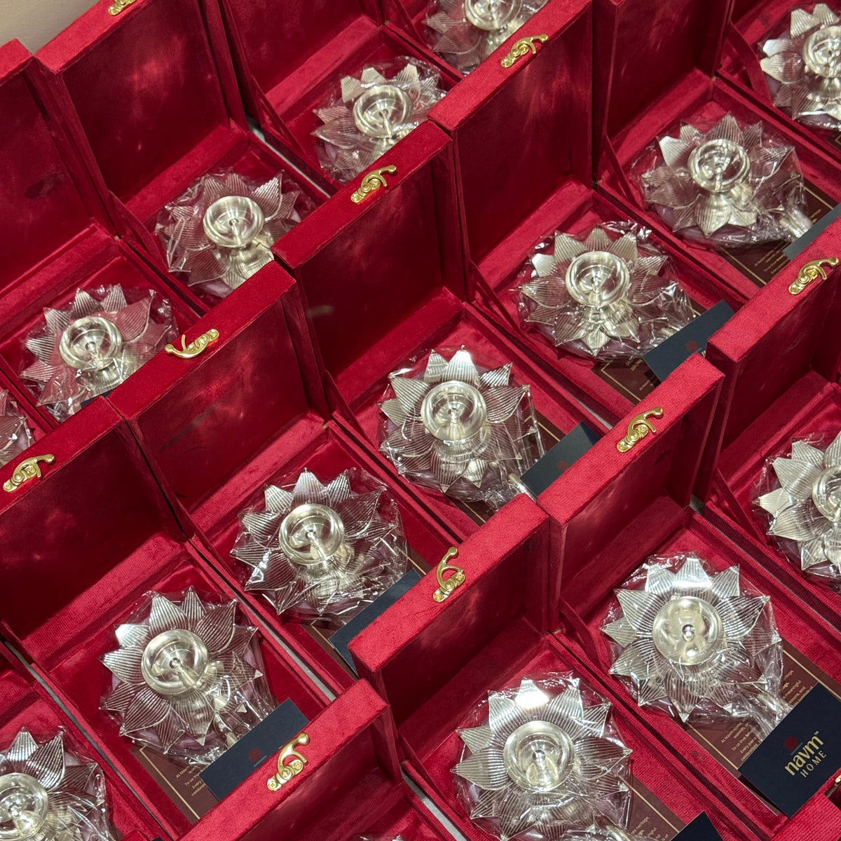 Multiple silver-toned lotus-shaped candle holders displayed inside open red gift boxes with gold trim and small black cards labeled FASHION.
