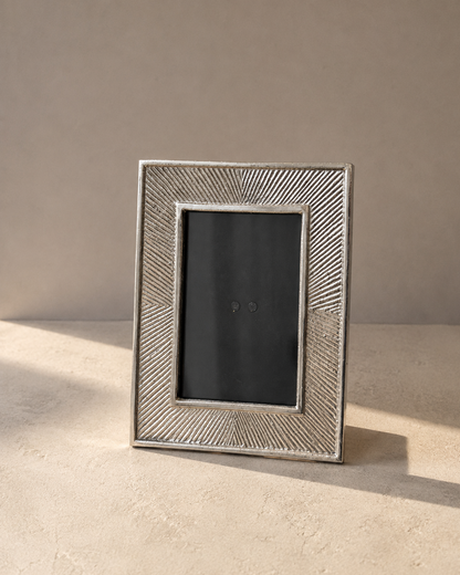 Navom Riva Silver Finished Aluminium Photo Frame standing on a minimalist beige luxury table showing fine chiseled lines under natural sunlight shadow