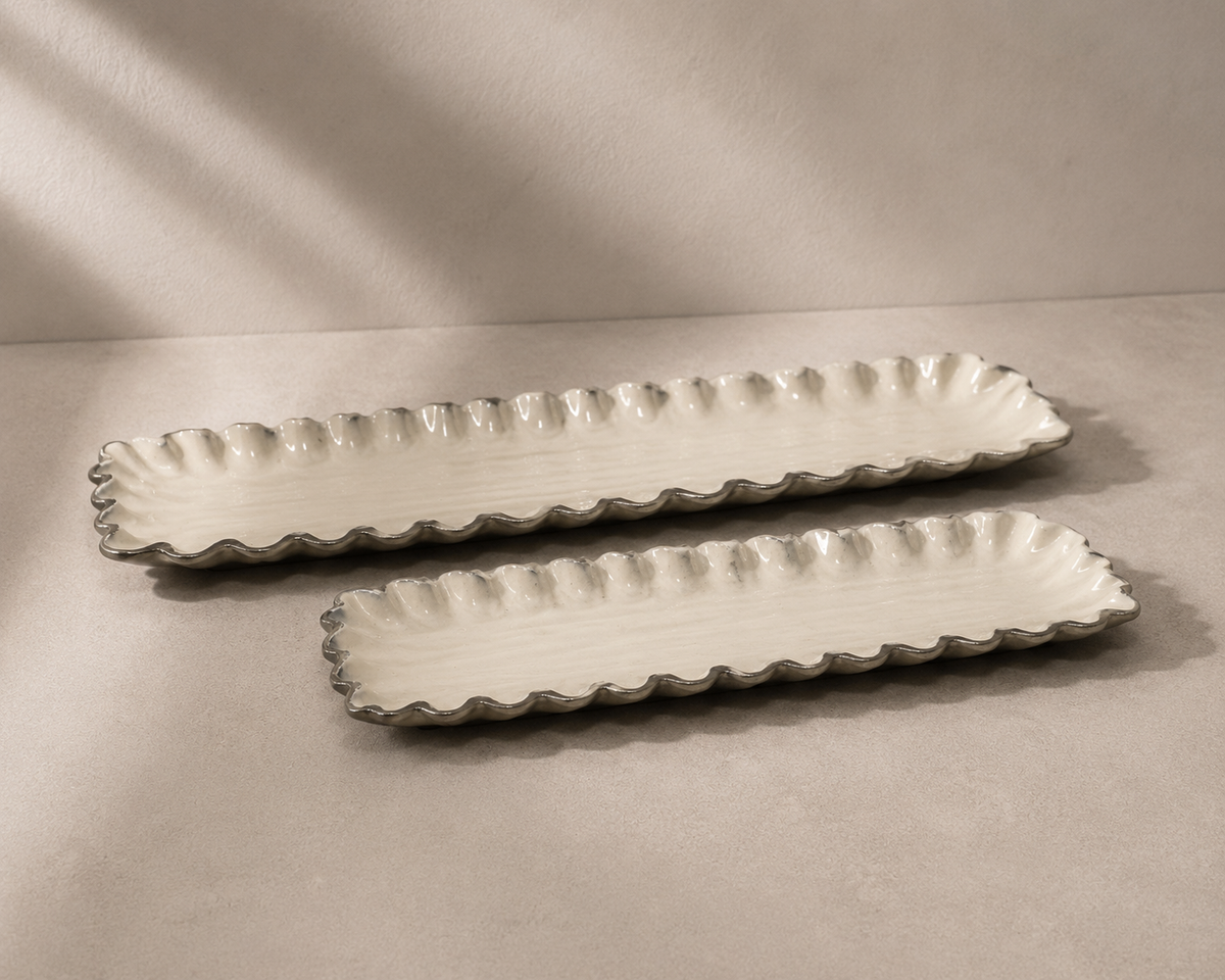Two long rectangular ceramic serving trays with scalloped edges, shown on a neutral beige surface with soft shadows.