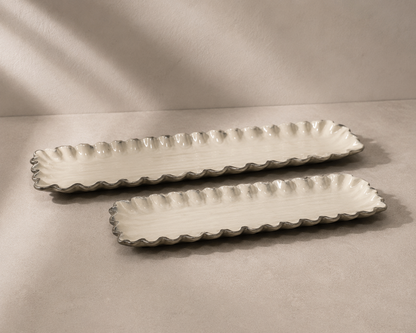 Two long rectangular ceramic serving trays with scalloped edges, shown on a neutral beige surface with soft shadows.